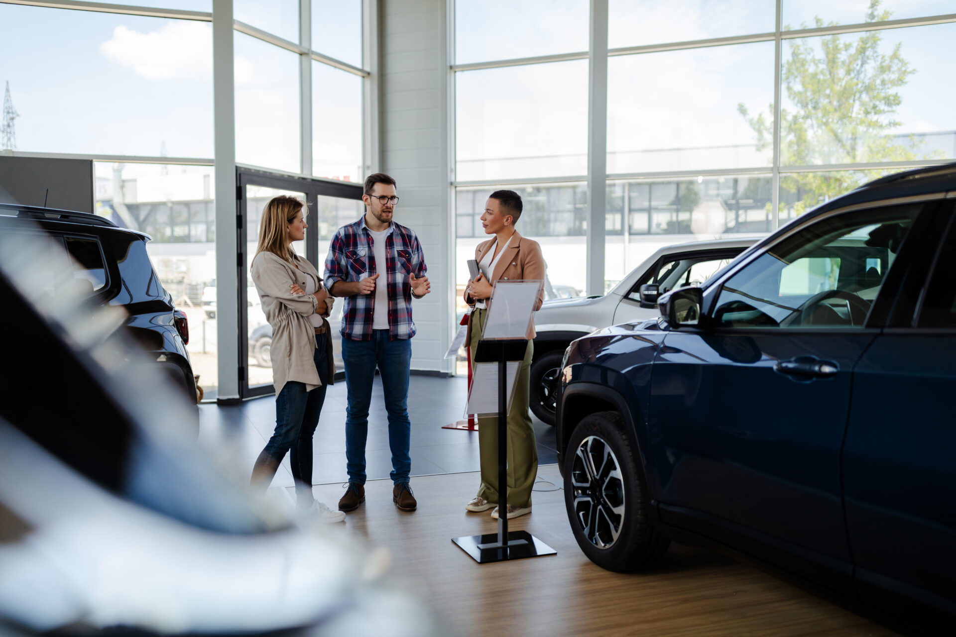Young female sales agent helping adult couple to choose a new car in modern car showroom | Warrantywise