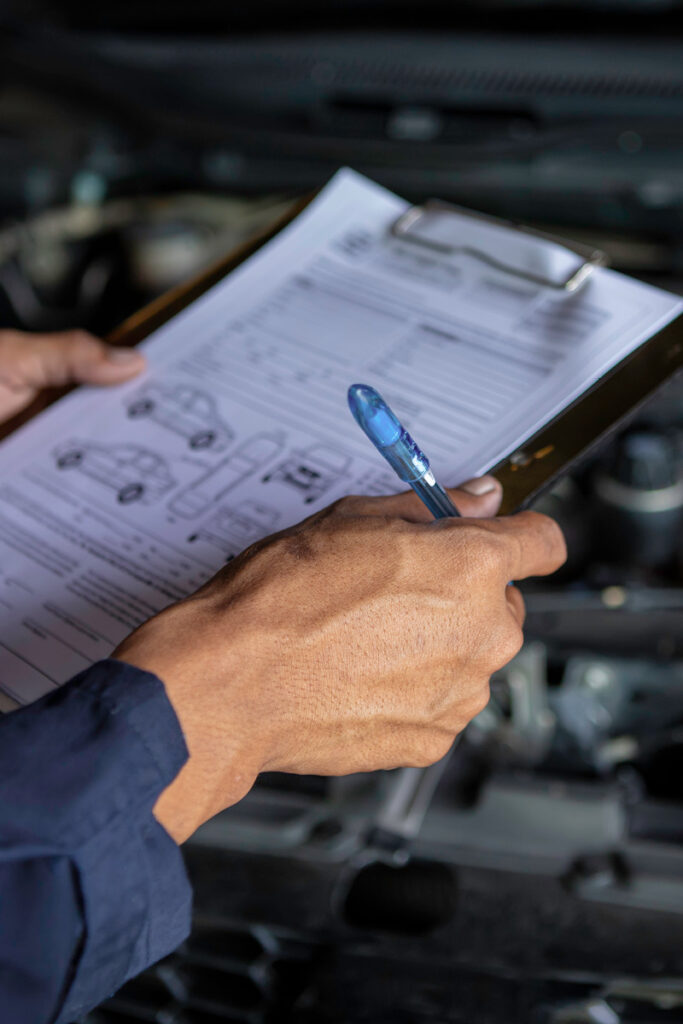 Car mechanic looking at inspection form in front of vehicle