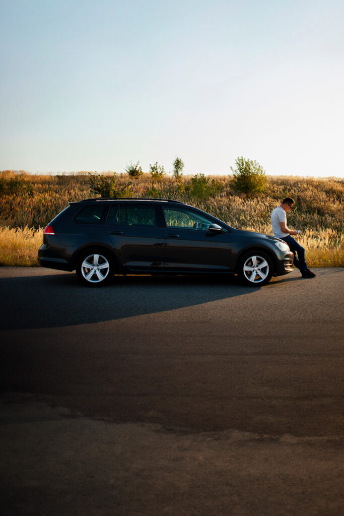 Man sitting on the bonnet of his car on his phone
