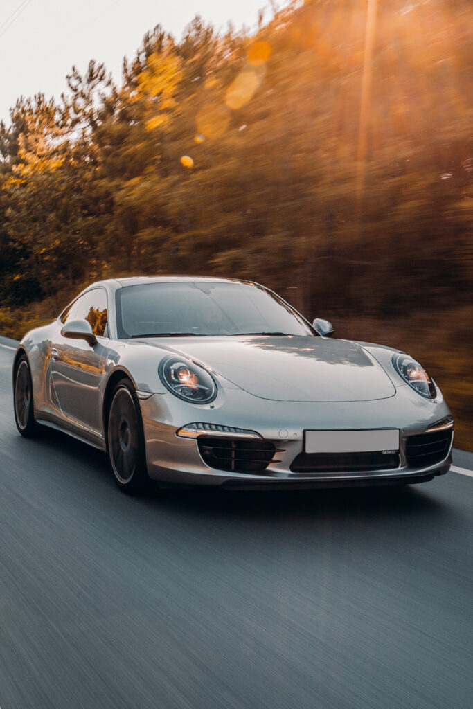 Porsche driving down a road with trees and sun in the background