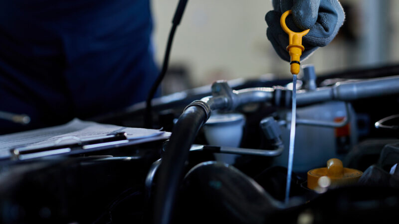 How to Check Your Car’s Engine Oil - Cover Photo | Warrantywise A person pours blue windshield washer fluid into a car’s engine compartment.