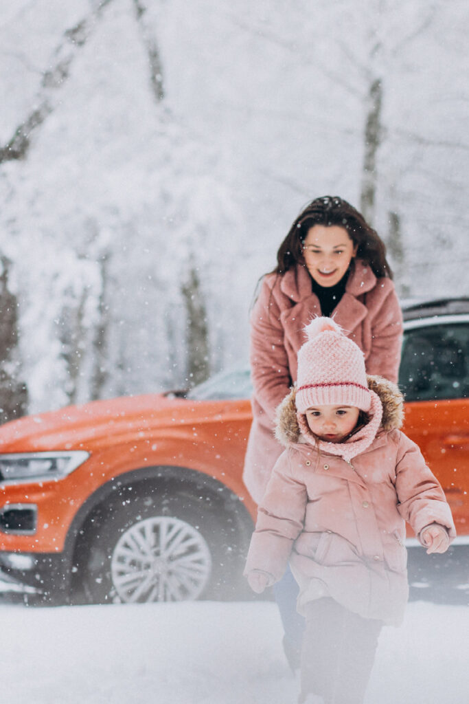 Little girl and mother walking in snow with car in the background
