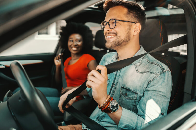 Young multiracial couple sitting in a car and fastening seat belts. | Warrantywise Young multiracial couple sitting in a car and fastening seat belts.