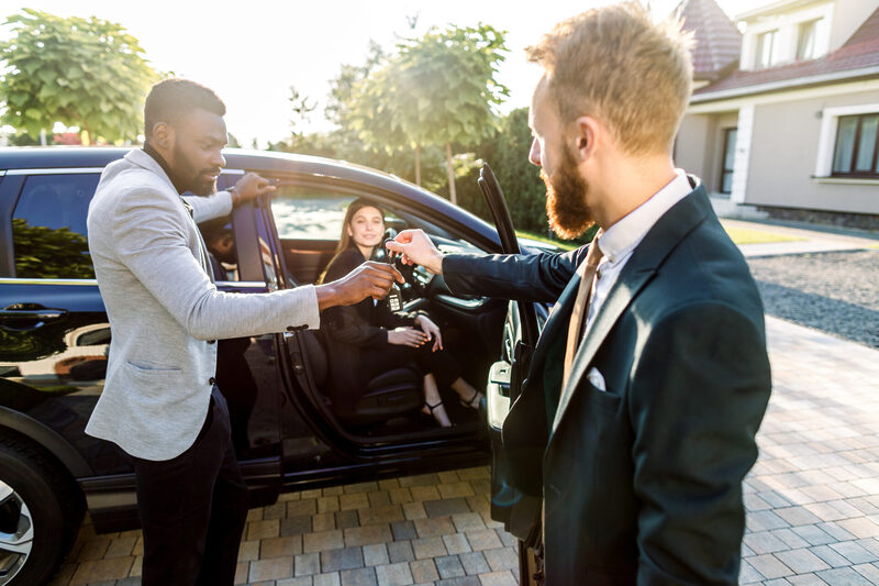 Young salesman handing car keys to young couple on a driveway