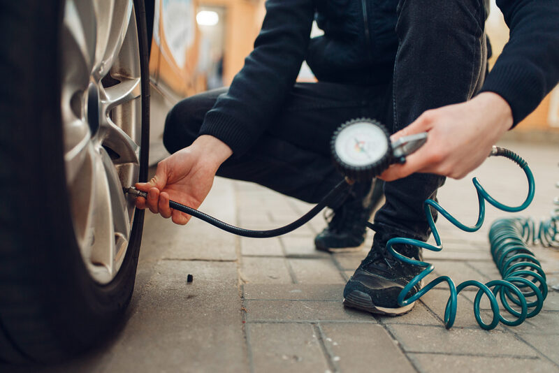 Male person checks the tire pressure, tyre service | Warrantywise Male person checks the tire pressure, tyre service. Vehicle repair service or business, man inflates the wheels on automobile outdoor