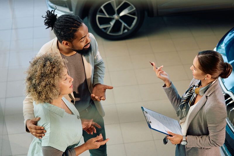 Young Couple and saleswoman talking at car dealership.
