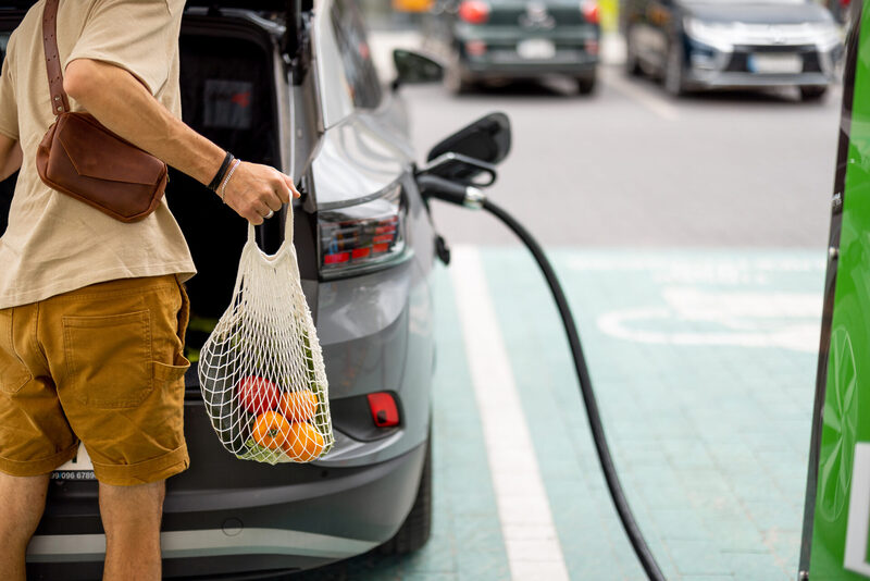 Man charging electric car while shopping | Warrantywise Man returning to charging electric car after shopping for fruit