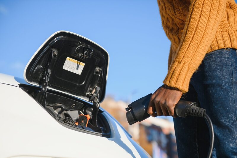 African American man charging his electric car. | Warrantywise African American man charging his electric car.