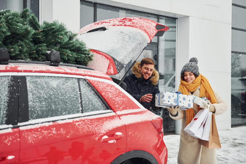 Young couple with gift boxes is near car with tree on the top
