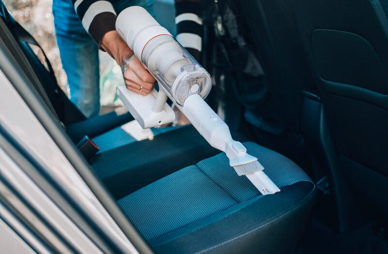 Close-up of a man vacuuming a car seat. The hand holds a cordles | Warrantywise Person vacuuming car seats. The hand holds a cordless vacuum cleaner and cleans the interior of the car.