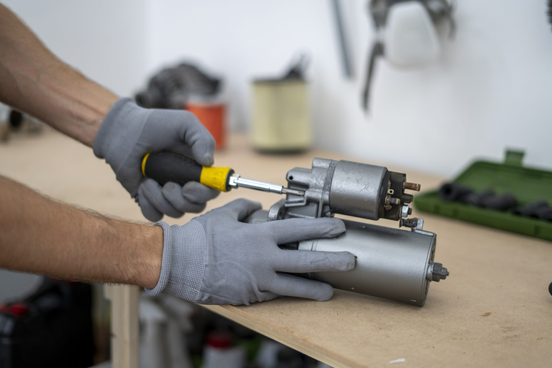 A person works on fixing a car starter using a screwdriver and wearing gloves in a well-lit workshop with a green toolbox present nearby | Warrantywise