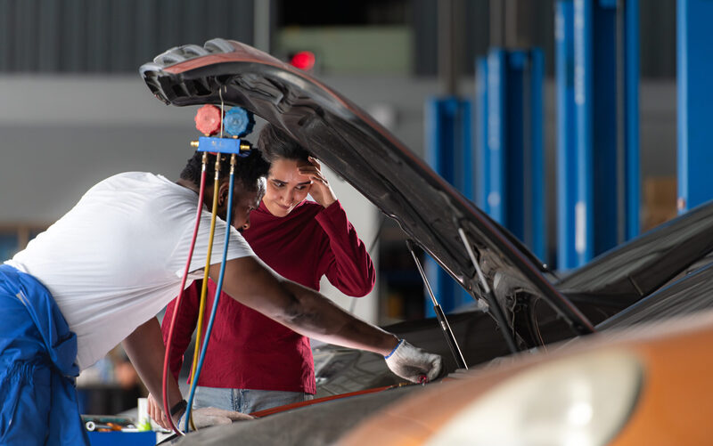 Car mechanic working in an auto repair shop explain to customer | Warrantywise Mechanic and concerned car owner checking over a car.