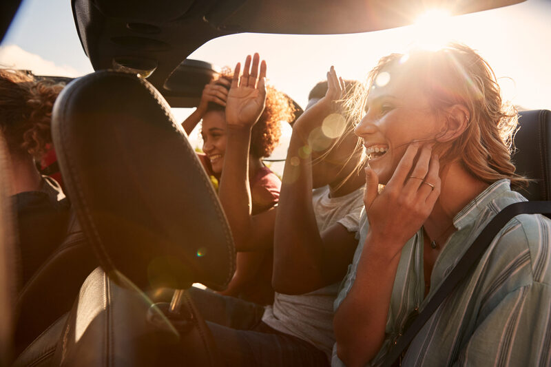 Happy young adult friends on a road trip vacation travelling in the back of an open car | Warrantywise