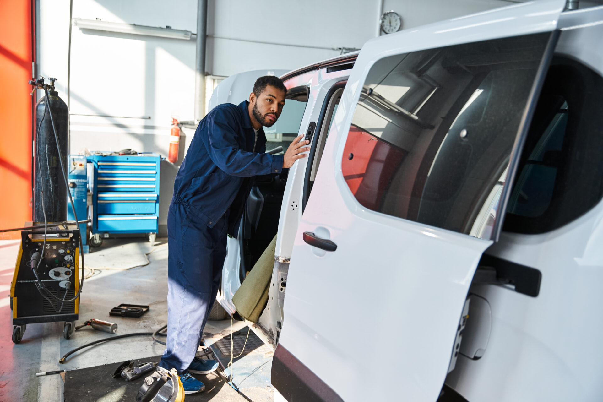 Young mechanic inspects a van while sunlight streams through the workshop windows | Warrantywise