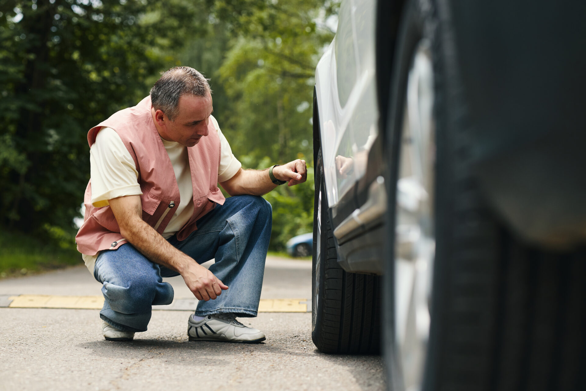 Middle Aged Caucasian Man Inspecting Car Tire during Family Road Trip Outdoors | Warrantywise