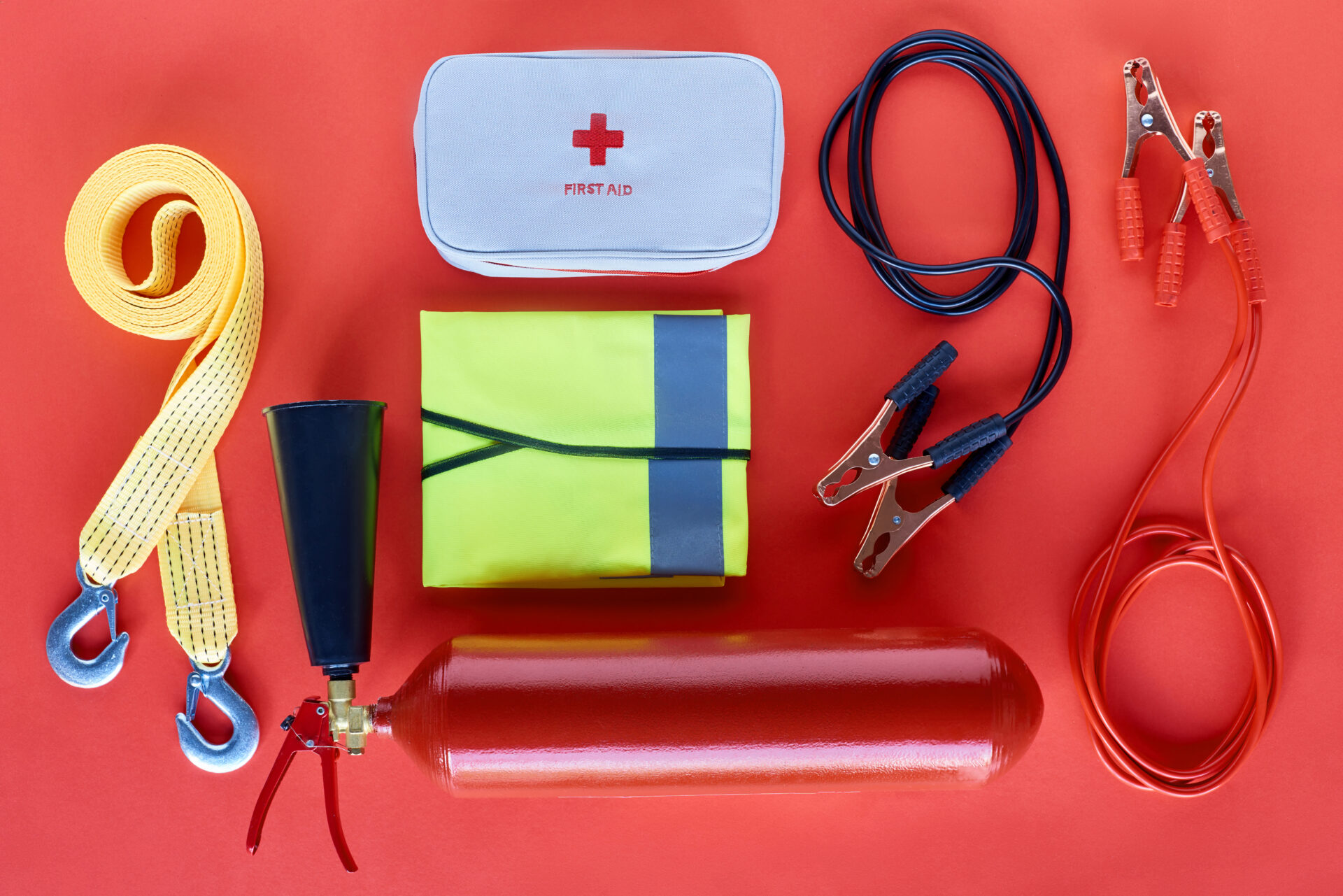 top view of fire extinguisher first aid kit and jump start cables on red background | Warrantywise