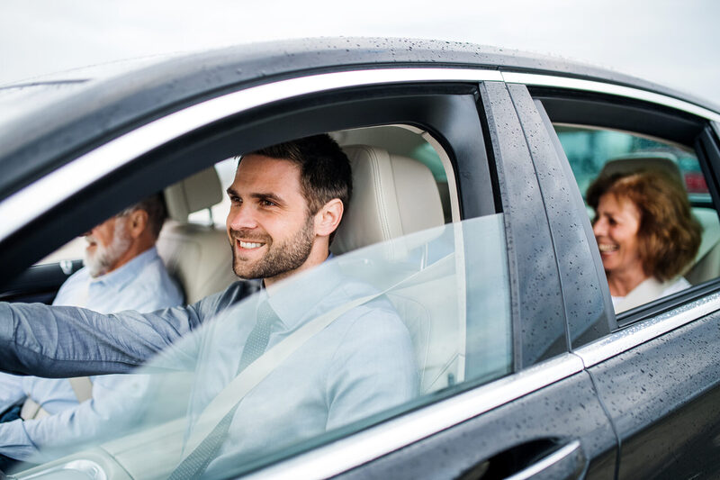 Mature son with senior parents sitting in car driving and talking | Warrantywise A smiling man drives a car with two passengers enjoying the ride.