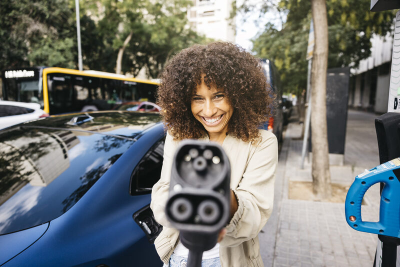 Playful woman charging an electric car on the street | Warrantywise