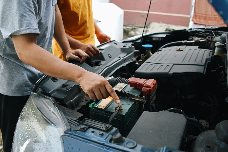 father-teaching-son-how-to-repair-and-check-car-en-2025-03-17-20-30-04-utc | Warrantywise Two people inspecting a car battery under the bonnet, checking electrical connections as part of routine vehicle maintenance.
